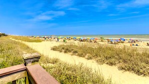 A beach with a wooden boardwalk, sandy dunes, and beach umbrellas.