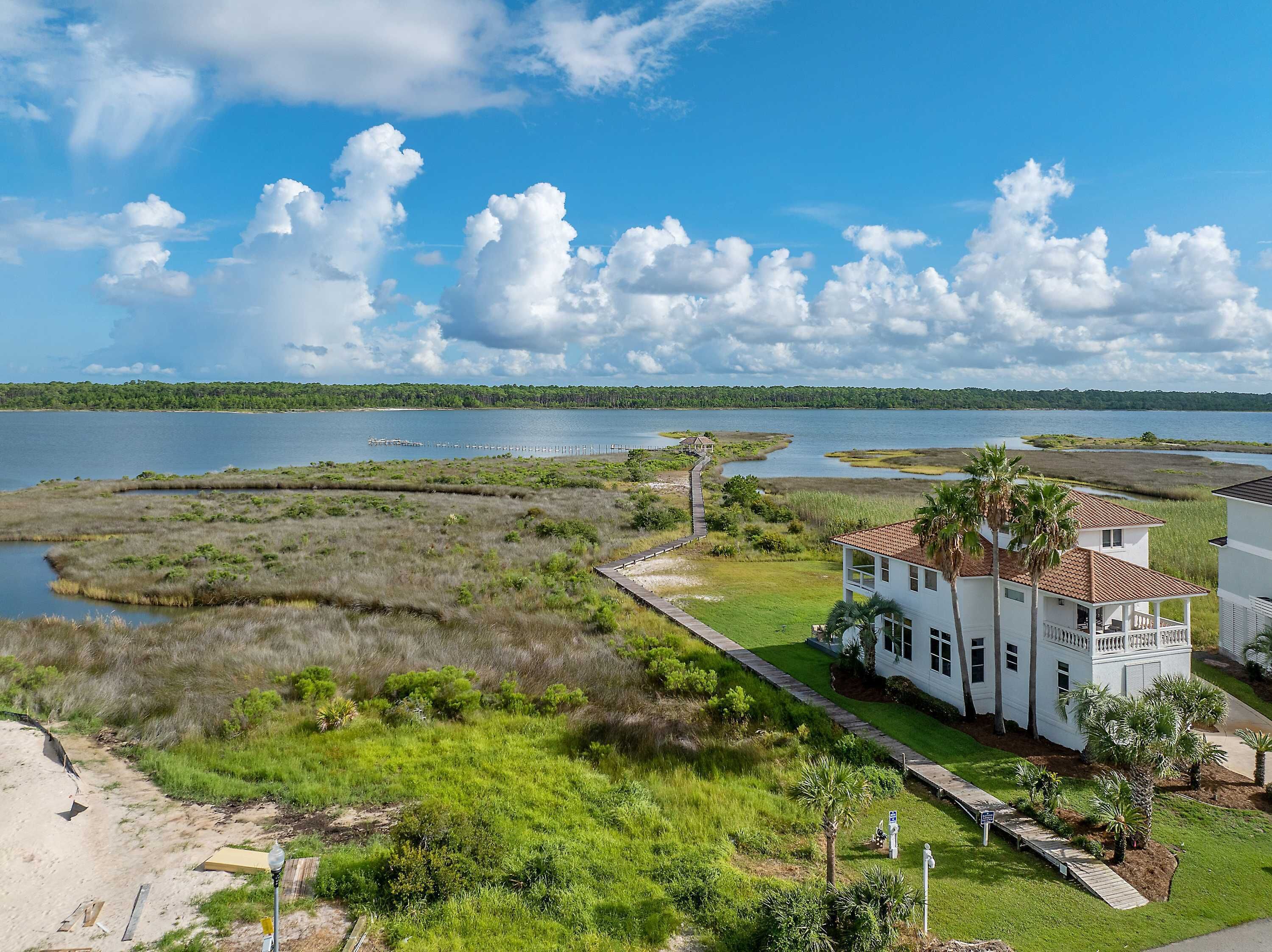 A white house with a red roof, surrounded by lush greenery and a view of a lake.