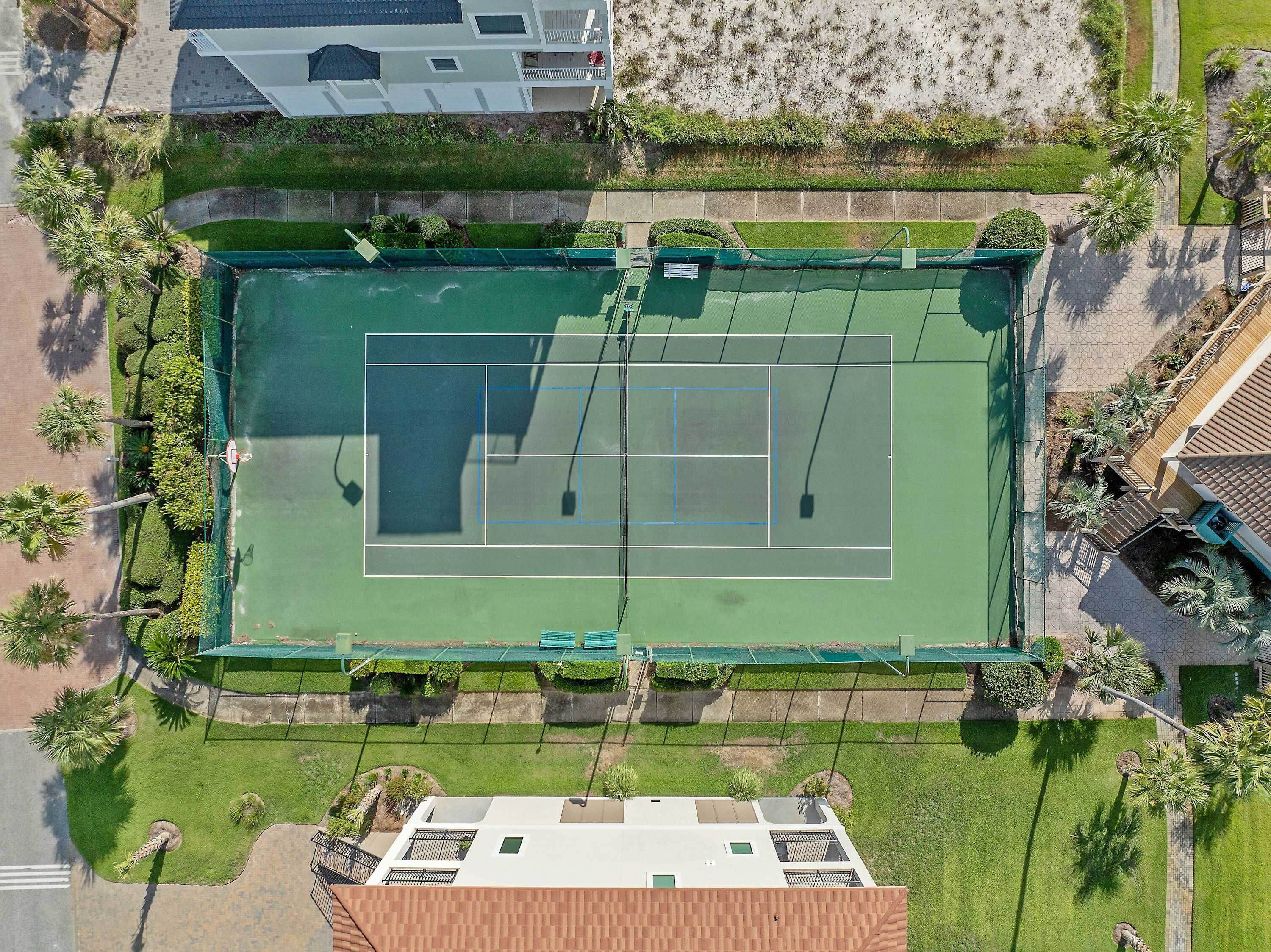 Ilmakuva tenniskentästä, jonka ympärillä on vehreää kasvillisuutta, ja sen lähellä sijaitsevasta rakennuksesta, jossa on parveke.