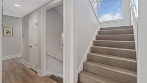 A staircase with carpeted steps leading to a landing, a white door, and a skylight above. - Laguna Sunset Elevator Beach Access (Gulf Shores)
