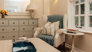 A bedroom with a bed, a dresser, a chair, a small table, and a window with a view of greenery. - Garden Lodge - pet friendly (Aston Tirrold)