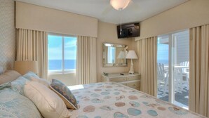 Une chambre à coucher comprenant un lit, une commode, un téléviseur et un balcon avec des chaises blanches.