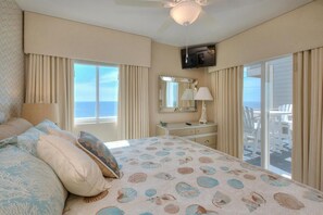 A bedroom with a bed, a dresser, a television, and a balcony with white chairs.