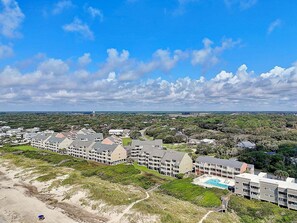 A coastal hotel with multiple buildings, a beach, and a clear sky.