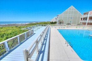 A pool area with a wooden deck, a clear blue pool, and a view of the ocean.