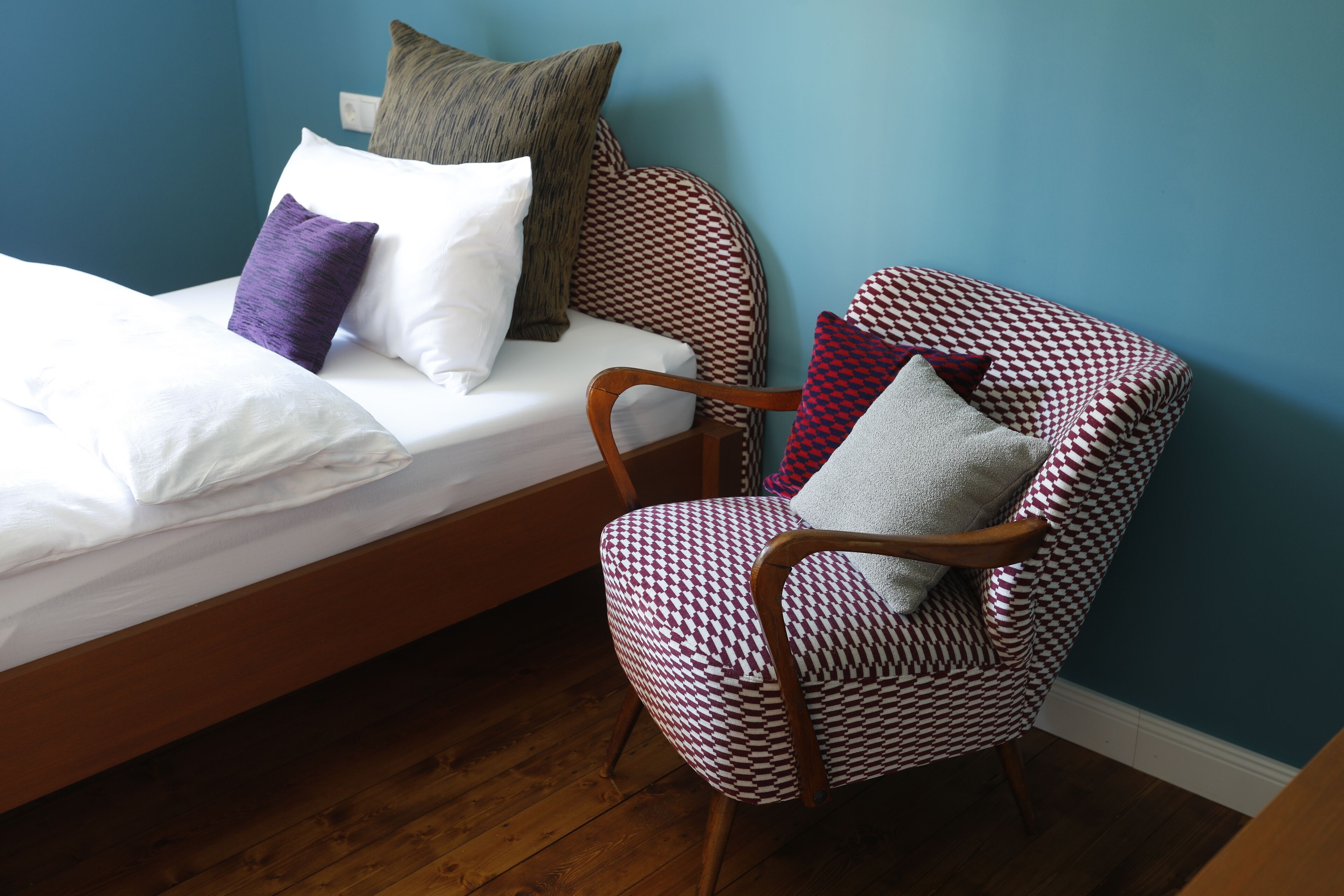 A bedroom with a wooden bed, a houndstooth patterned armchair, and a blue wall.