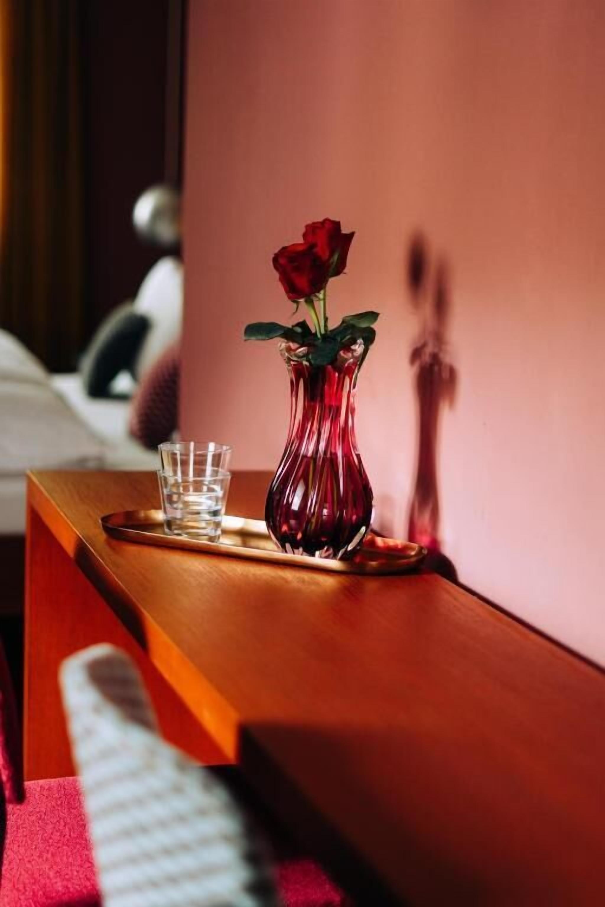 Un comodino in legno con un vaso rosso contenente una rosa e un bicchiere d'acqua.