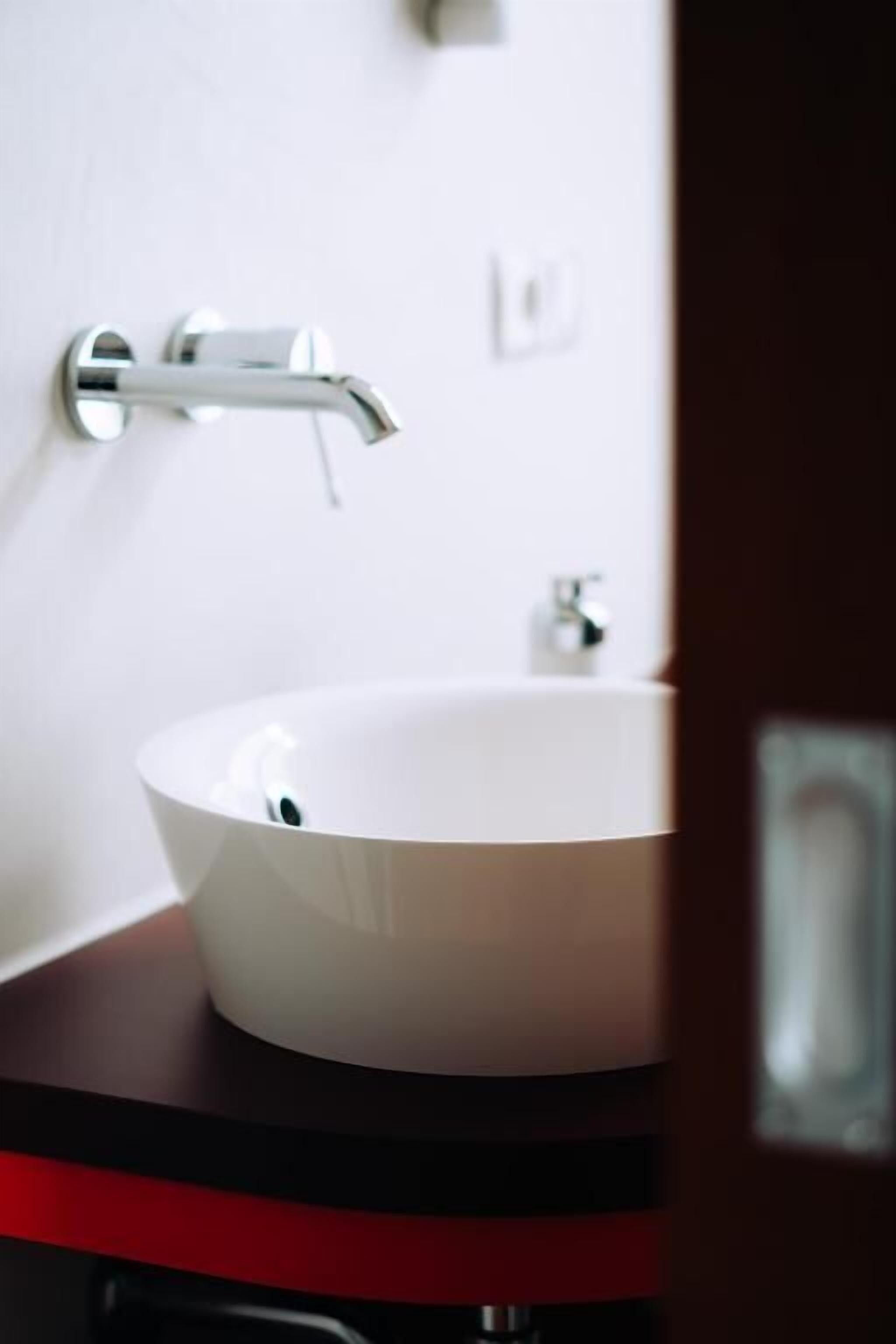 Une salle de bain moderne avec un lavabo blanc, un robinet chromé et un plan de toilette rouge.