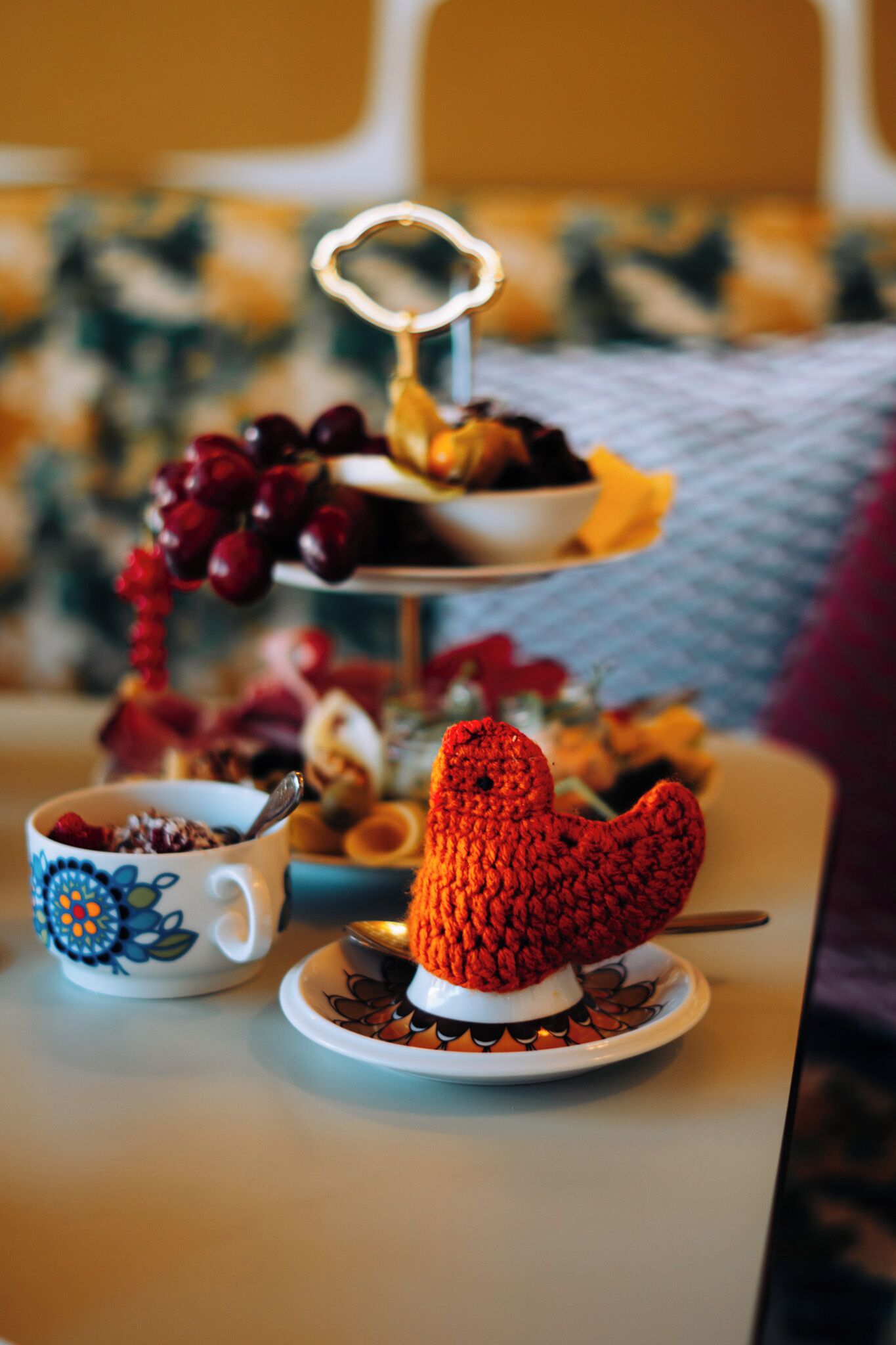 Una mesa con un pájaro decorativo, una bandeja de frutas y una taza con una cuchara.