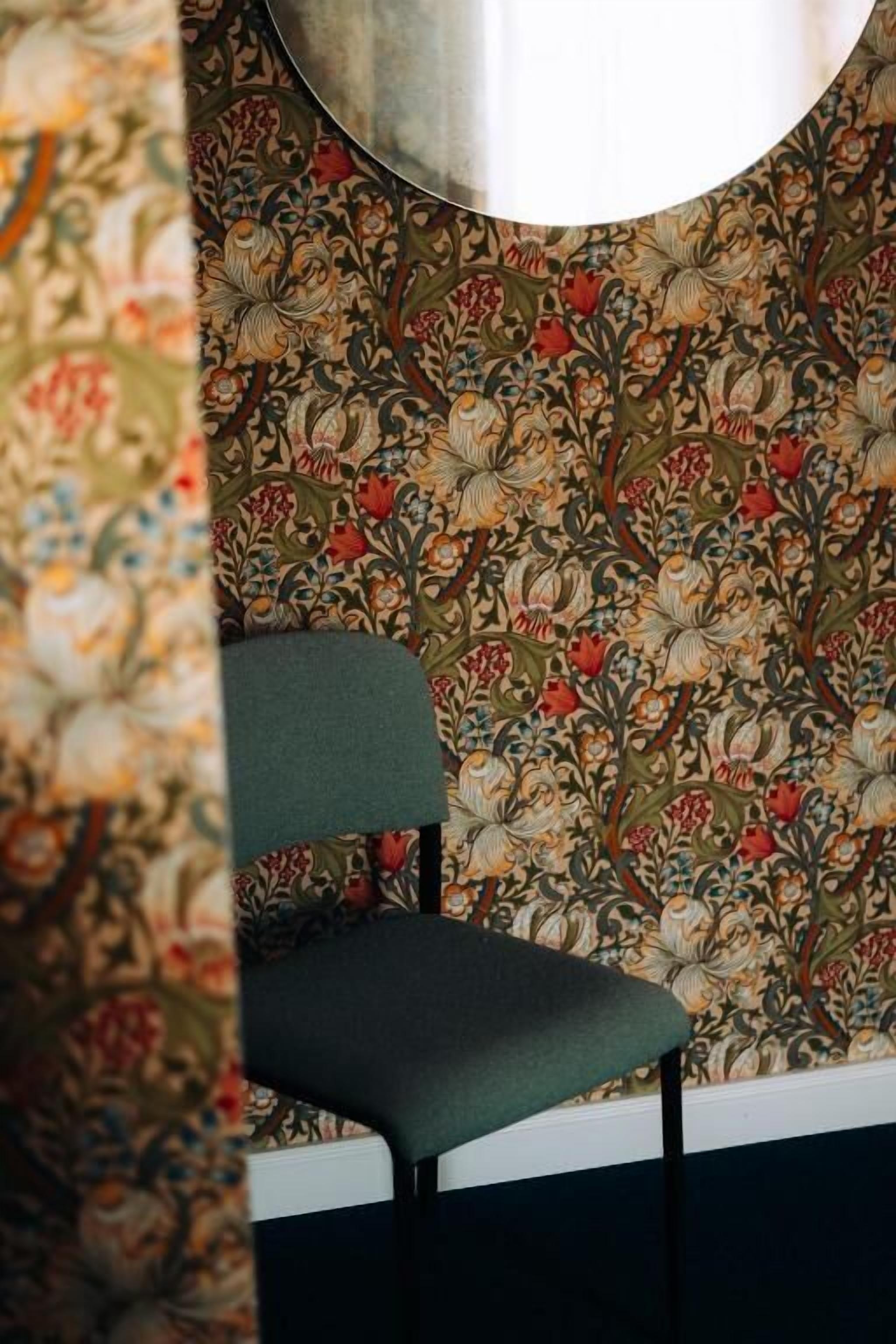 Een kamer met bloemenbehang, een groene stoel en een witte plint.