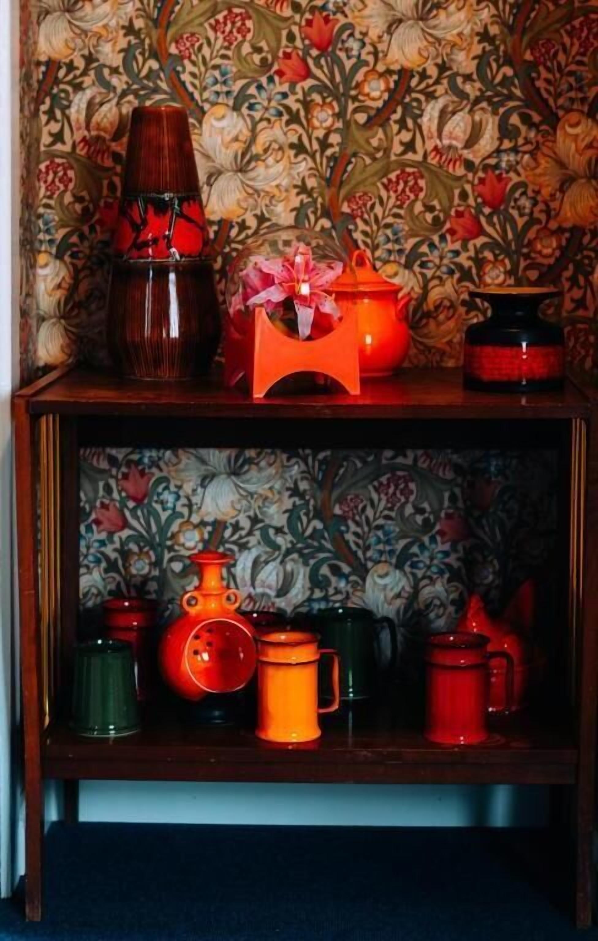 Una estantería de madera con varios utensilios de cocina, incluyendo un hervidor rojo, una tetera verde y una taza roja.
