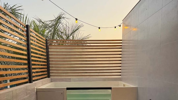 Een moderne buitenruimte met een ingebouwd bubbelbad, een houten schutting met spijlen en een betegelde vloer.