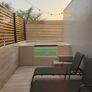 Un espace extérieur moderne, aménagé avec un coin salon, un jacuzzi intégré, une clôture en bois à lattes et un sol carrelé.