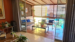 Een moderne woonkamer met een glazen deur die leidt naar een balkon, een bank, een bijzettafeltje en verschillende planten.