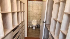 Een smalle gang met houten wandplanken aan weerszijden, die leidt naar een badkamer met toilet en betegelde muren.