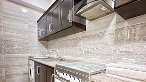 A modern kitchen with dark wooden cabinets, a stainless steel stove, and a built-in oven. - Margarita Hotel Amman (Amman)