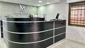 A hotel reception desk with a modern design, a logo above the desk, and a window with a metal grille. - Margarita Hotel Amman (Amman)