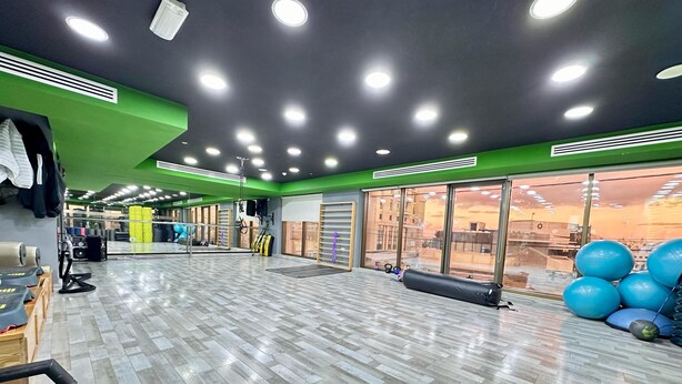 A spacious gym with a herringbone-patterned floor, mirrored walls, and a large window with a city view. - Margarita Hotel Amman (Amman)