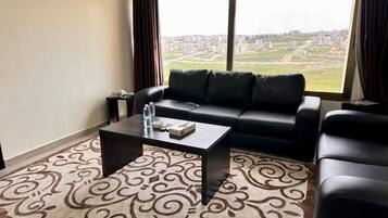A living room with a black leather sofa, a coffee table, and a view of a cityscape through large windows.