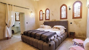 Un dormitorio con una cama grande, ventanas en arco y un taburete pequeño.