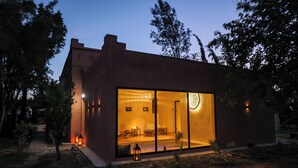 Un edificio moderno con amplios ventanales de vidrio, un interior visible con mobiliario y un exterior bien iluminado.