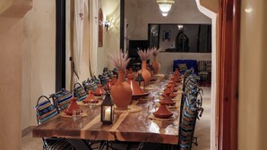Una larga mesa de comedor con numerosas sillas, jarrones ornamentales y una araña.