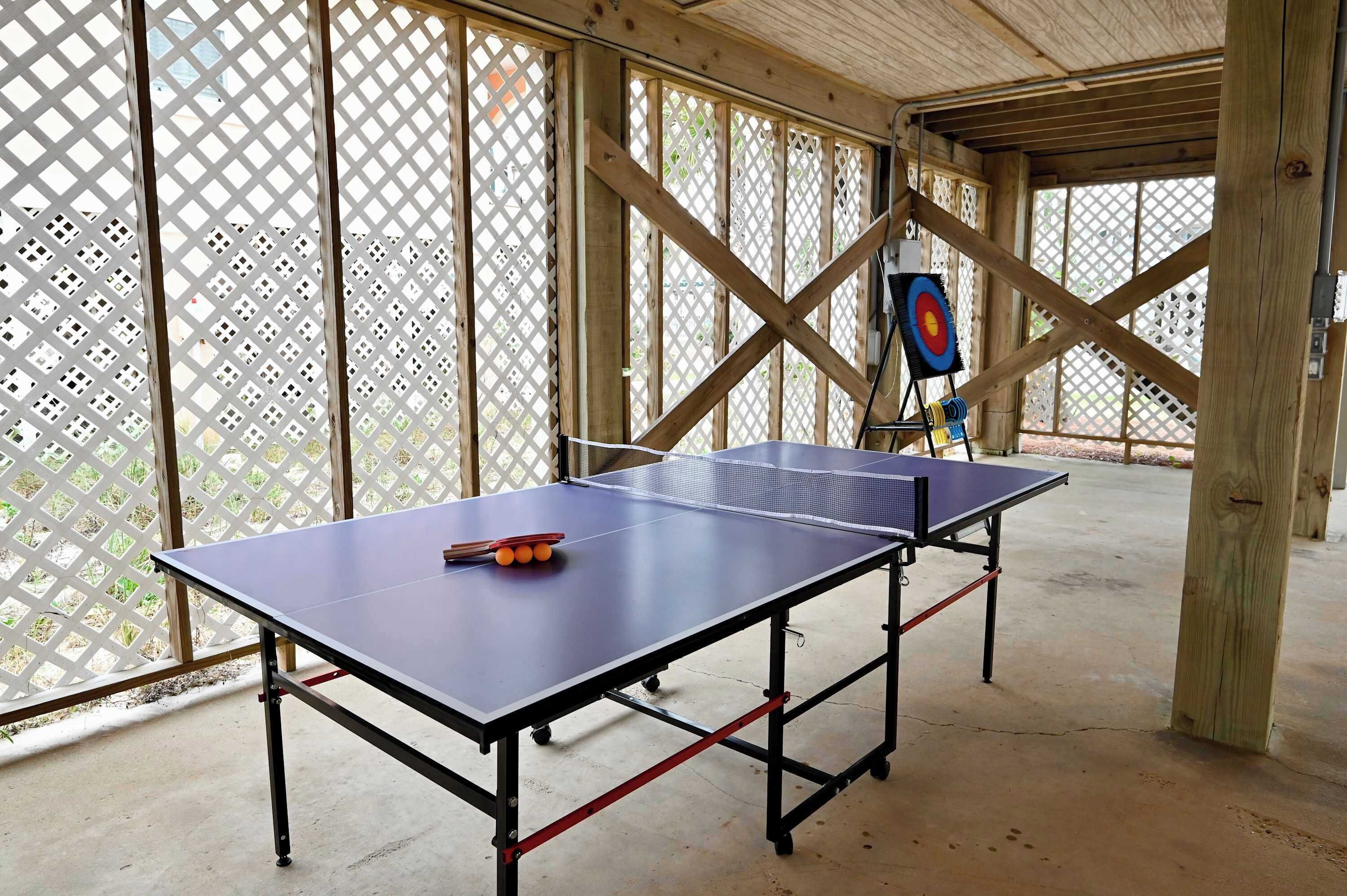 Una mesa de ping pong con red y pelotas, instalada en un espacio interior con paredes de celosía de madera y techo.