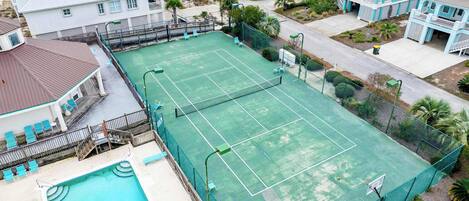 A tennis court with a pool and a building with a balcony.