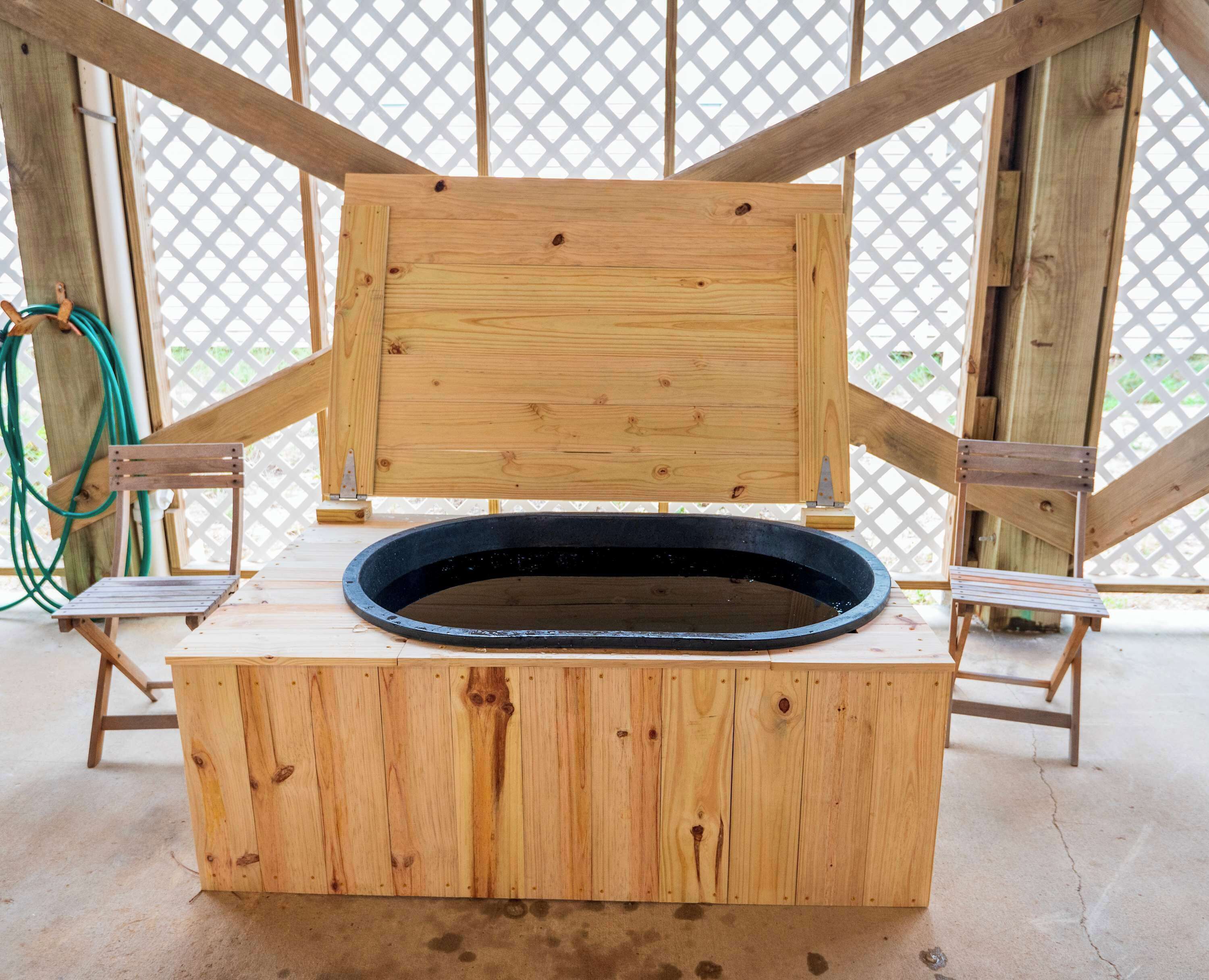 A wooden structure with a raised platform and a circular basin, possibly a sauna or hot tub, in a room with a lattice window.