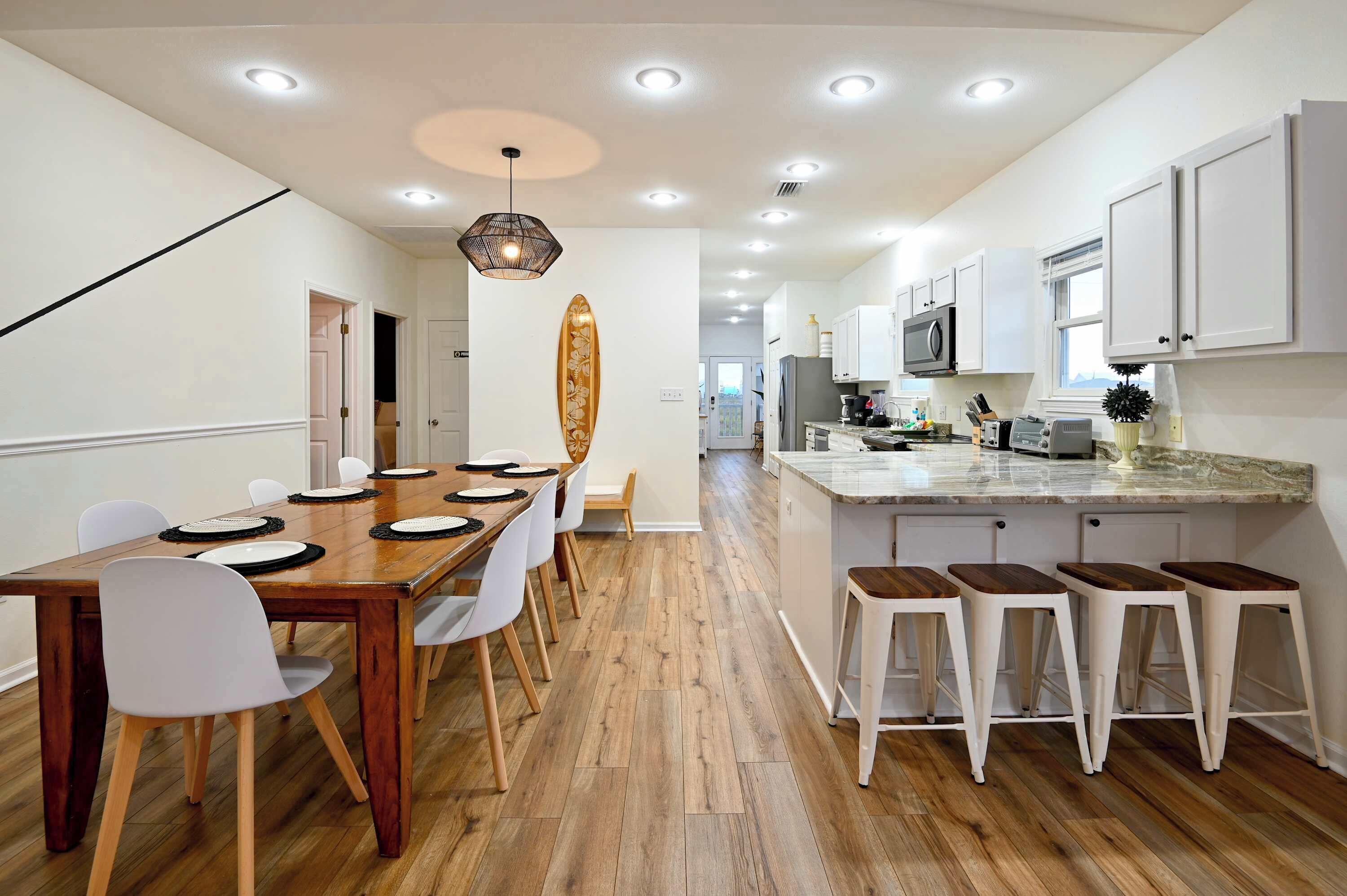 Een moderne keuken met witte kasten, een houten eettafel met witte stoelen en een houten bar met krukken.