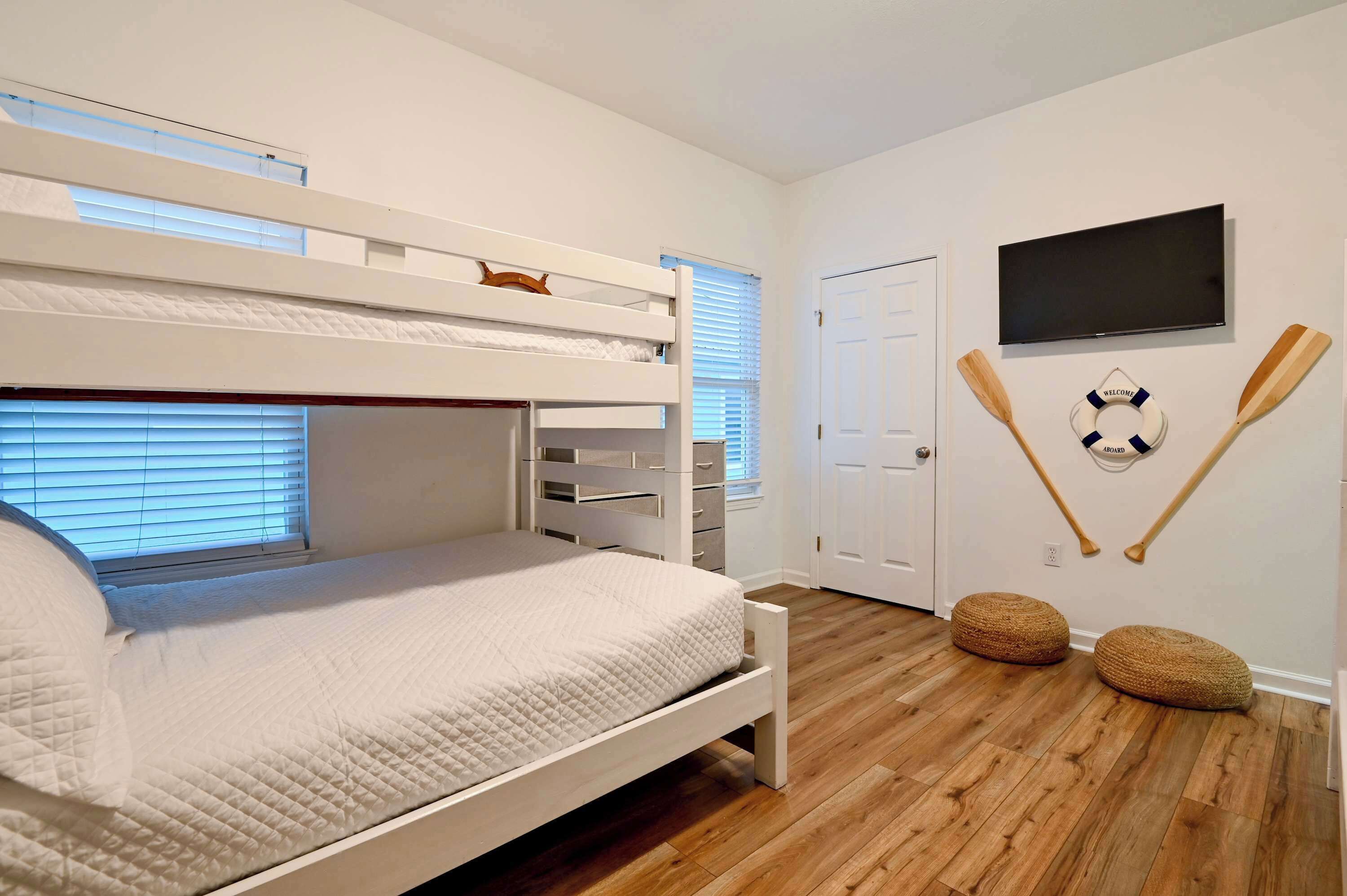 A bunk bed with a TV mounted on the wall, wooden bats, and a welcome mat.