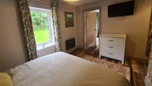A bedroom with a bed, a dresser, a television, and a window with curtains.