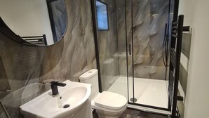 A modern bathroom with a marble wall, a white sink, a toilet, and a glass shower enclosure.