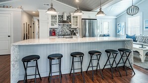 Une cuisine moderne dotée d’un îlot en marbre, de tabourets de bar, de luminaires suspendus et d’un réfrigérateur en acier inoxydable.