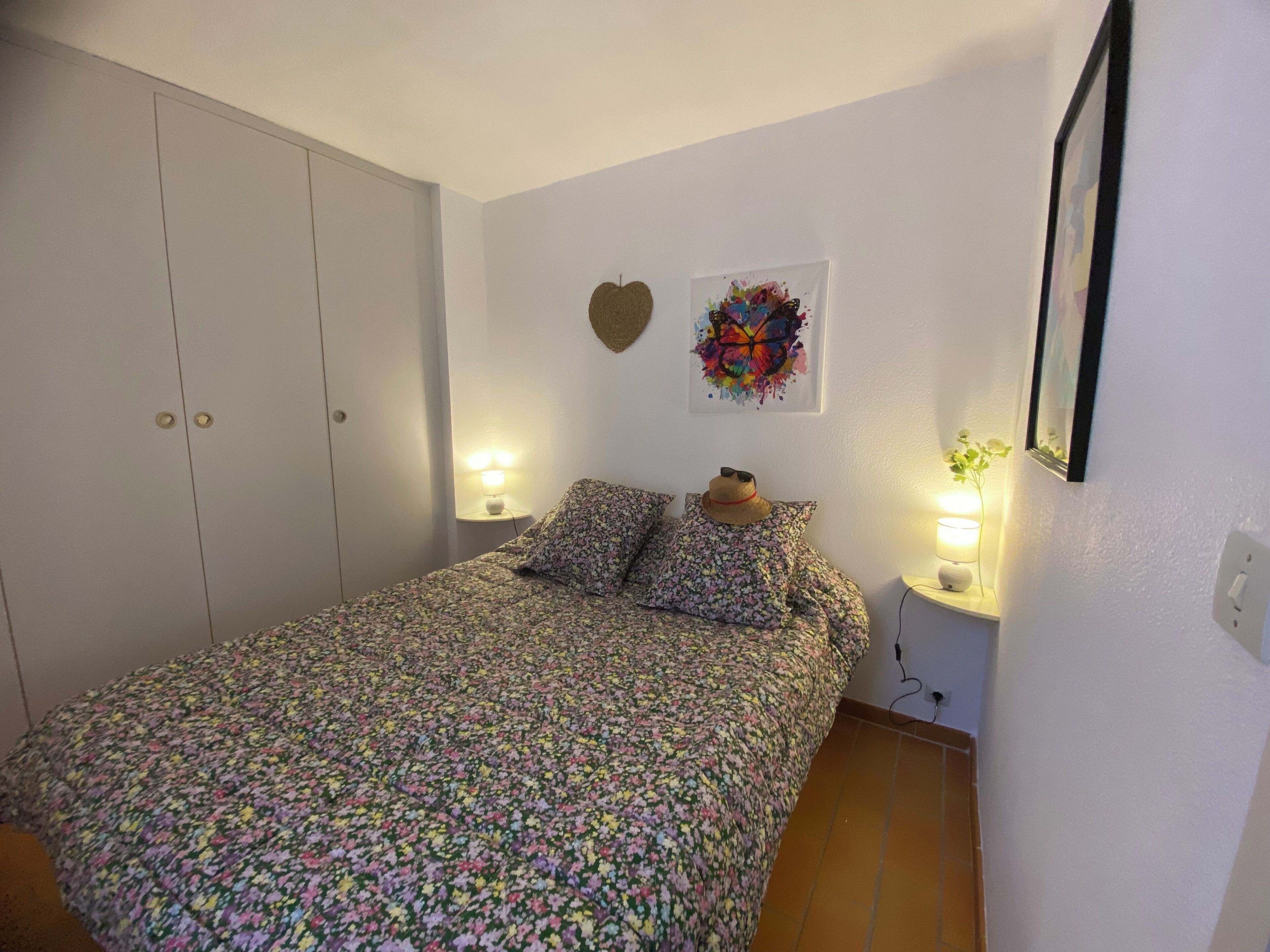 Een slaapkamer met een bed, een kledingkast, een nachtkastje, een wanddecoratie en een spiegel.