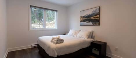 Un dormitorio con cama, una mesita de noche, una ventana y un cuadro en la pared.