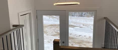 A staircase with a wooden handrail and black balusters, leading to a door with a view of a snowy landscape.