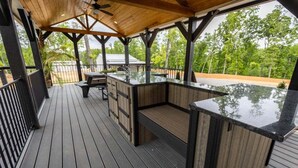 An outdoor deck with a wooden floor, a built-in bar area, and a covered seating area. - The Salt Shack ("In The Pines" at KY Lake) | 121 Pine Grove Lane, Dover, TN 37058 (Dover)