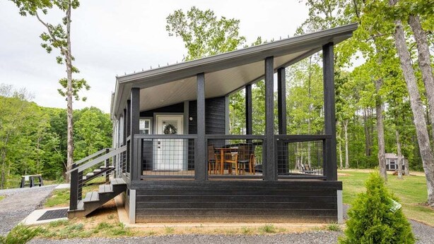 Una cabana moderna amb un porxo cobert, una escala que condueix a l'entrada i vistes de la forest circumdant.