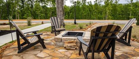 A stone patio with Adirondack chairs and a fire pit.