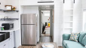 A compact kitchen with white cabinetry, a stainless steel refrigerator, and a wooden coffee table.