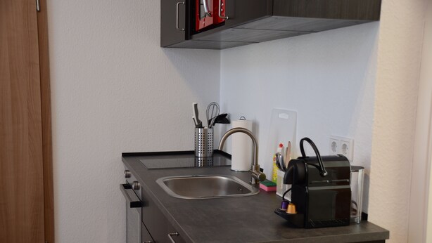 Eine kleine Küche mit Spüle, einer Kaffeemaschine und einem Messerset auf der Arbeitsplatte.