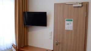 Ein Zimmer mit einem Holztisch, einem Stuhl, einem an der Wand montierten Fernseher und einer Tür mit einem Schild.