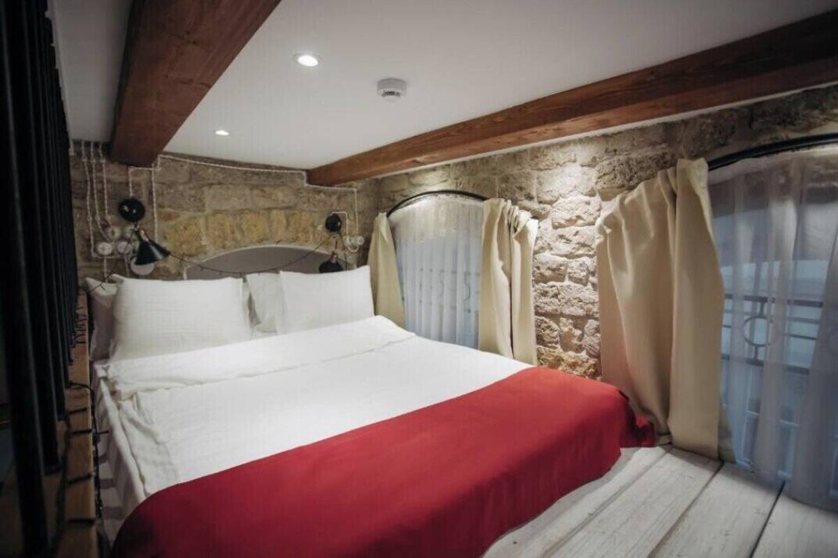 Une chambre à coucher avec un lit, des murs en pierre, des poutres en bois et une fenêtre avec des rideaux.