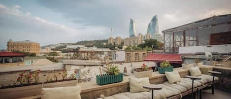 A rooftop terrace with outdoor seating, a view of the cityscape, and a building with a distinctive blue facade.