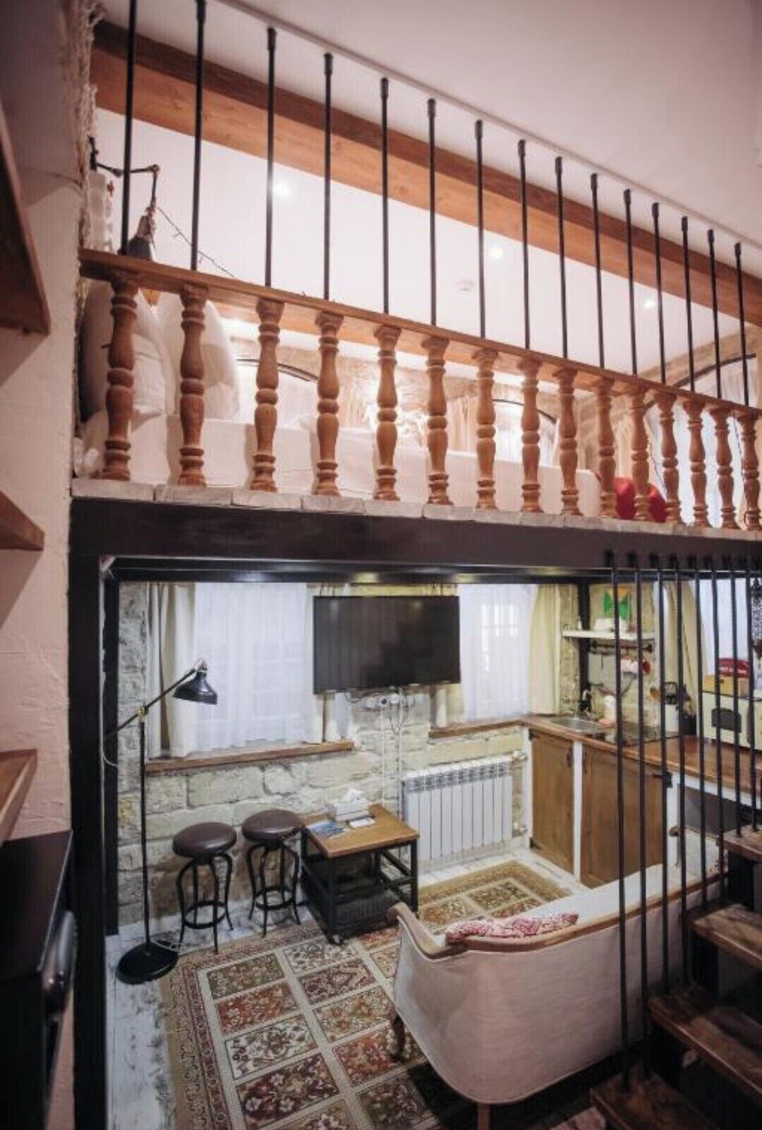 A room with a wooden staircase, a dining area with stools, a radiator, and a television.
