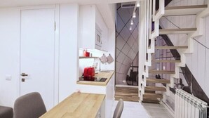 Eine moderne Küche mit einem Holztisch und -stühlen, einem roten Wasserkocher und einer Treppe mit geometrischem Wanddesign.