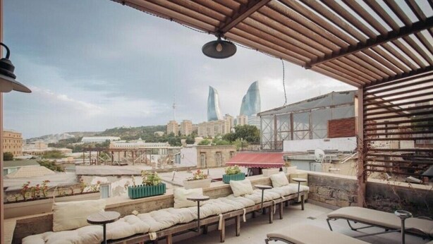 Eine Dachterrasse mit Sitzgelegenheiten im Freien, einem Pavillon und Blick auf die Stadtlandschaft, darunter zwei markante Gebäude.