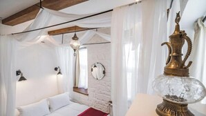 Ein Schlafzimmer mit einem Bett, weißen Vorhängen, einer Hängelampe und einem dekorativen Messingobjekt auf einem Tisch.