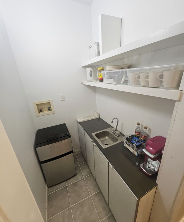 Una kitchenette compacta con refrigerador, lavamanos y estantes de almacenamiento.